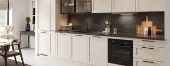 Moderne Einbauküche in elegantem, zeitlosem Design mit cremefarbenen Rahmenfronten, dunkler Arbeitsplatte und schwarzen Griffen. Die Küchenzeile bietet harmonische Kontraste zwischen hellen Oberflächen und einer dunklen Rückwand.